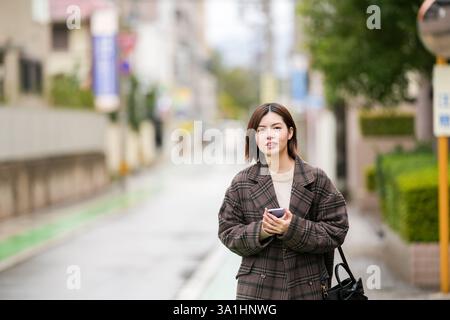 Eine 29-jährige Japanerin in einem karierten Mantel. Sie läuft durch Gassen mit wenigen japanischen Autos in der Hand. Stockfoto