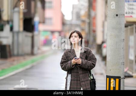 Eine 29-jährige Japanerin in einem karierten Mantel. Sie läuft durch Gassen mit wenigen japanischen Autos in der Hand. Stockfoto