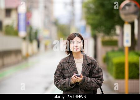 Eine 29-jährige Japanerin in einem karierten Mantel. Sie läuft durch Gassen mit wenigen japanischen Autos in der Hand. Stockfoto