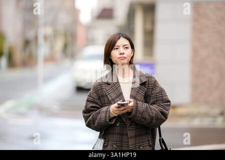 Eine 29-jährige Japanerin in einem karierten Mantel. Sie läuft durch Gassen mit wenigen japanischen Autos in der Hand. Stockfoto