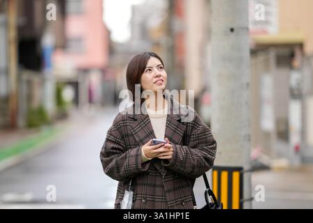 Eine 29-jährige Japanerin in einem karierten Mantel. Sie läuft durch Gassen mit wenigen japanischen Autos in der Hand. Stockfoto