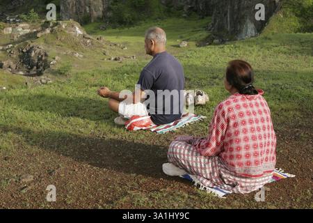 Pärchen mittleren Alters, die morgens auf einem frischen grünen Feld sitzen und Atemübungen machen, die „Pranayam“ genannt werden, Indien KEIN MR Stockfoto