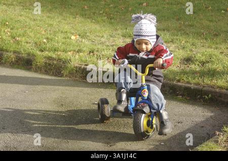 Ein kleiner, zweieinhalb Jahre alter Junge, der ein Dreirad fährt und Wintertücher trägt. MR. # 468 Stockfoto