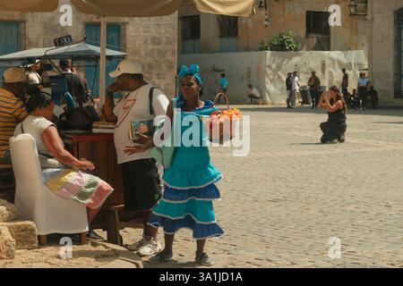 Havanna, Kuba 2024 April 17 - Straßenszene mit Verkäuferin und Kubanerin auf dem plaza Square, Old Havanna. Frau in farbenfroher traditioneller Kleidung namens R Stockfoto