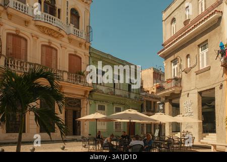 Havanna, Kuba, 2024. April 17. Touristen, die in einem Café im Freien auf einer plaza, Plazuela de Santo Ángel, vor schönen alten Kolonialgebäuden sitzen Stockfoto