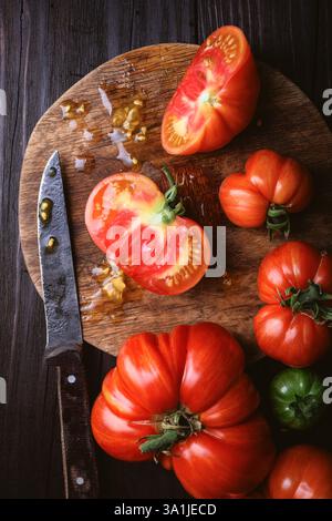 Frische und saftige Tomaten, geschnitten auf rundem Holzschneidebrett. Altes Messer und rustikaler Holztisch. Lebensmittelfotografie von oben Stockfoto