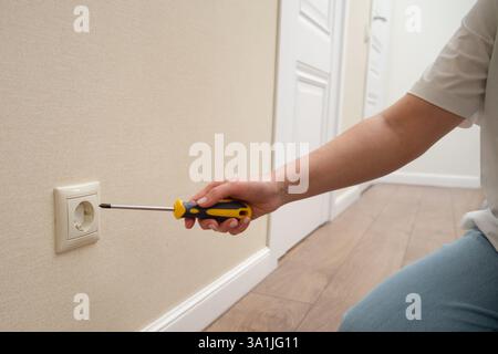 Person, die die Steckdose mit einem Schraubendreher an der beigefarbenen Wand repariert. Hauswartung und elektrisches Arbeitskonzept Stockfoto