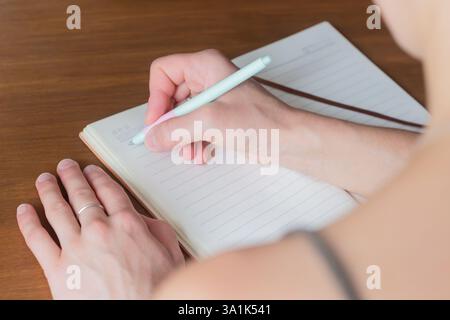 Eine Nahaufnahme einer Hand, die einen Stift hält und in ein offenes Tagebuch schreibt. Das Foto zeigt das Wesen einer durchdachten Planung und persönlichen Reflexion Stockfoto