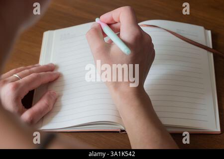 Eine Nahaufnahme einer Hand, die einen Stift hält und in ein offenes Tagebuch schreibt. Das Foto zeigt das Wesen einer durchdachten Planung und persönlichen Reflexion Stockfoto