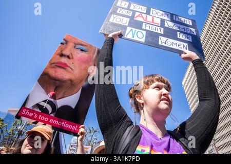 Los Angeles, Usa. März 2025. Die Demonstranten halten Plakate, die ihre Meinung zum Ausdruck bringen, während sie zum Frauenmarsch in Los Angeles auf den Straßen der Innenstadt von Los Angeles fahren. Quelle: SOPA Images Limited/Alamy Live News Stockfoto