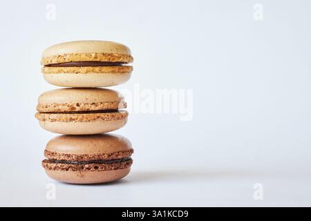 Stapel von drei braunen französischen Macarons, Kuchen mit verschiedenen Geschmacksrichtungen, Kaffee und Creme Brulee Geschmack. Pyramide mit hausgemachtem Dessert, Makronen, Seitenansicht, Stockfoto