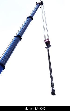 Blauer Kranarm vertikal, Ausleger mit Hängehaken gegen klaren Himmel. Bau und Heben von schweren Baustoffen, großen Bauteilen und Maschinen. Stockfoto