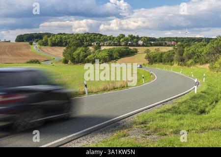 Autofahren auf gewundenen Landstraßen durch grüne Felder unter blauem Himmel mit Wolken im Frühling, Thüringen, Deutschland, Europa Stockfoto