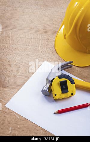 Bleistift-Tapeline-Hammer-Papierhelm auf Holzbrett Stockfoto