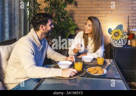 Ein lächelndes Paar frühstückt zusammen auf dem Balkon und genießt die Gesellschaft und eine gesunde Mahlzeit Stockfoto