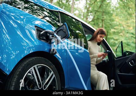 Die junge Frau sitzt in einem Elektroauto, das auflädt. Stockfoto