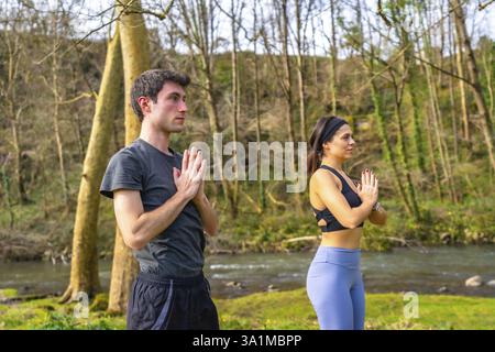 Yogalehrer spielen eine Baumpose an einem Fluss in einem Wald und genießen die Ruhe der Natur Stockfoto