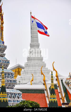 Bangkok, Thailand - 4. Mai 2009: Die thailändische Nationalflagge erhebt sich über Wat Phra Kaews kunstvoller, goldener Architektur, ein Symbol für kulturellen Stolz und Intrige Stockfoto