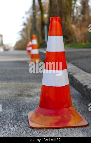 Eine Linie von leuchtend orangefarbenen Verkehrskegeln steht auf einer Asphaltstraße und markiert eine Grenze oder einen eingeschränkten Bereich. Stockfoto