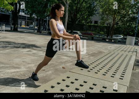 Sportliche Frau in Sportbekleidung, die Beine vor dem Laufen in einem Stadtpark dehnt Stockfoto