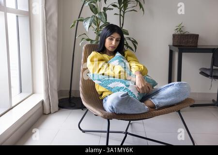 Die indische Frau sitzt im Sessel und sieht melancholisch, verärgert und unglücklich aus Stockfoto