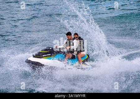 Junge Erwachsene auf einem Sea-Doo Wasserflugzeug, das in der Straße von Tāmaki zwischen Auckland und Waiheke Island in Aotearoa, Neuseeland, durch die Wellen stürzt. Stockfoto