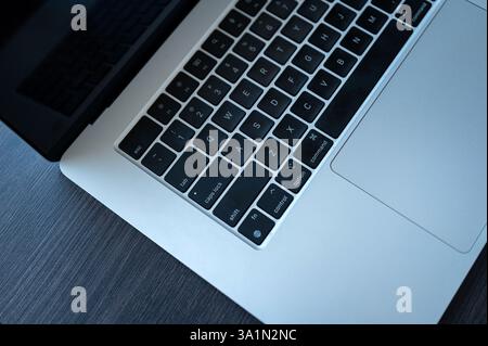 Nahaufnahme einer MacBook-Tastatur und eines Trackpads auf einem dunklen Holzpult mit schwarzen Tasten, Aluminiumgehäuse und partieller Bildschirmreflexion Stockfoto