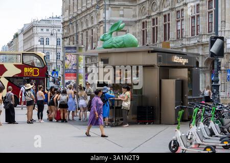 Touristen am Bitzinger Würstelstand Albertina in Wien an einem Sommernachmittag mit grünen Hasenskulpturen, E-Scootern und Sightseeing-Bus in der Nähe Stockfoto