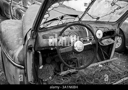 Ein Blick auf das Innere eines alten Autos auf einem Schrottplatz, der die relativ primitiven Konsolen über den freiliegenden Sitzfedern zeigt. Stockfoto