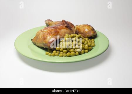 Im Ofen gebratenes Hähnchenschenkelviertel mit Erbsen auf großer grüner Platte. Auf weißem Hintergrund, mit Beschneidungspfad Stockfoto