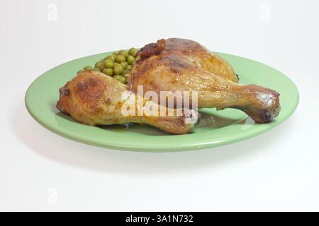 Im Ofen gebratene Hähnchenschenkelviertel und Hähnchenkeulen mit grünen Erbsen, auf großer Platte. Auf weißem Hintergrund, mit Beschneidungspfad Stockfoto
