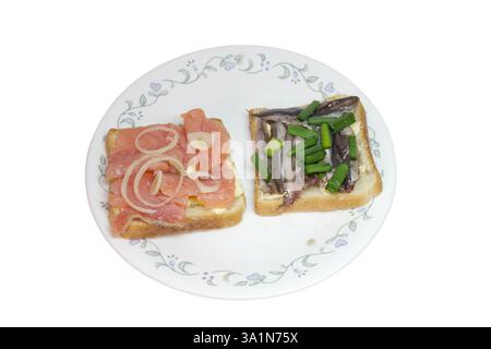 Scheiben von gesalzenem Lachs und geräucherter Sprotte, auf weißem Toastbrot mit Butter, abgeschmeckt mit gehackten Schalotten. Paar Sandwiches auf weißer Porzellanplatte Stockfoto