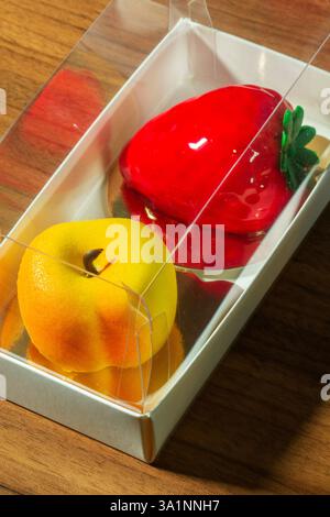 Geschenkset Mousse-Kuchen in Form von Früchten und Beeren in einer Box. Karton mit Kuchen in Form eines Pfirsichs und einer Erdbeere auf einem Tisch in Stockfoto