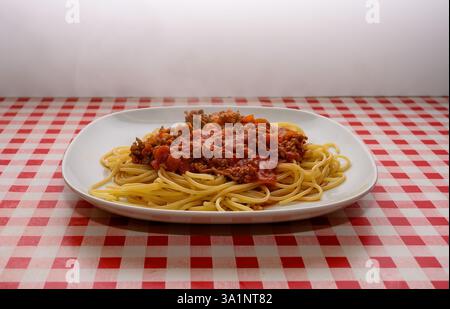 Eine großzügige Portion Spaghetti mit reichhaltiger Fleischsauce wird auf einem weißen Teller serviert. Die markante rot-weiße karierte Tischdecke verleiht dem Besucher einen besonderen Touch Stockfoto