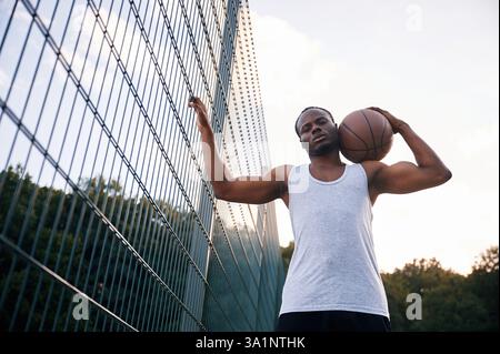 Ansicht von unten. Der junge Schwarze ist draußen mit Basketball. Stockfoto