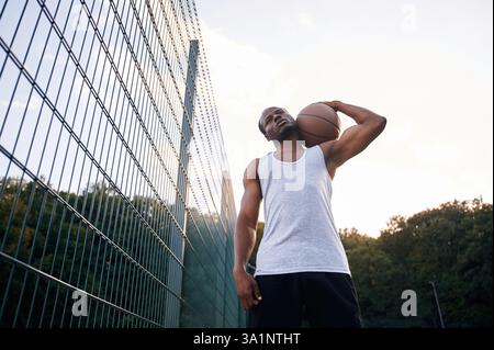 Ansicht von unten. Der junge Schwarze ist draußen mit Basketball. Stockfoto