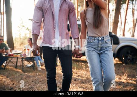 Nahaufnahme eines Paares, das sich mit Händen hält. Eine Gruppe von Freunden ist zusammen im Wald. Stockfoto