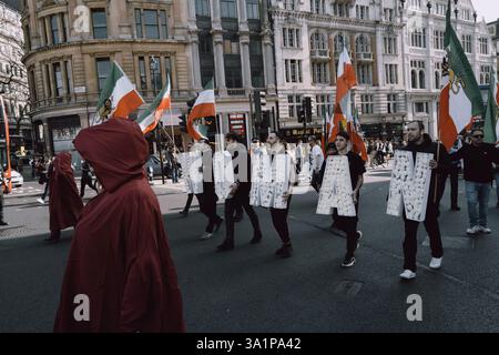 Am Internationalen Frauentag, 8. März 2024, marschierten britisch-iranische Frauen, organisiert von der Gruppe Stage of Freedom, schweigend durch das Zentrum Londons, gekleidet in roten Mänteln und weißen Hauben, die an das Märchen der Magd erinnern. Die Prozession begann am Parlamentsplatz und endete in der iranischen Botschaft in Kensington. Die Teilnehmer trugen Plakate von Demonstrantinnen, die seit Beginn der „Mahsa-Proteste“ im September 2022 vom iranischen Regime getötet, verletzt oder inhaftiert worden waren, ausgelöst durch den Tod der 22-jährigen Mahsa Amini während der Haft der iranischen Moralpolizei. Die Kleidung Stockfoto