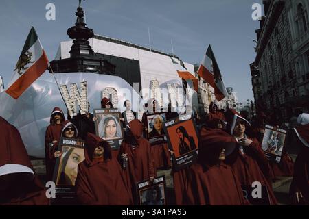 Am Internationalen Frauentag, 8. März 2024, marschierten britisch-iranische Frauen, organisiert von der Gruppe Stage of Freedom, schweigend durch das Zentrum Londons, gekleidet in roten Mänteln und weißen Hauben, die an das Märchen der Magd erinnern. Die Prozession begann am Parlamentsplatz und endete in der iranischen Botschaft in Kensington. Die Teilnehmer trugen Plakate von Demonstrantinnen, die seit Beginn der „Mahsa-Proteste“ im September 2022 vom iranischen Regime getötet, verletzt oder inhaftiert worden waren, ausgelöst durch den Tod der 22-jährigen Mahsa Amini während der Haft der iranischen Moralpolizei. Die Kleidung Stockfoto