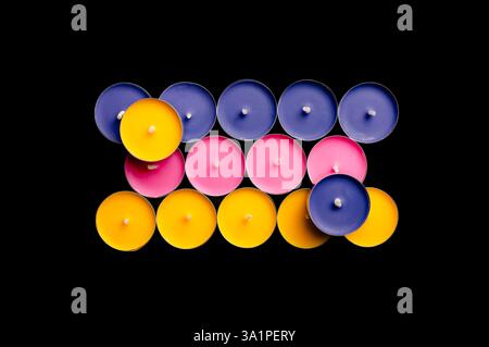 Teelichter in Rosa, Gelb und Blau, in einer verspielten Komposition vor einem krassen schwarzen Hintergrund. Stockfoto