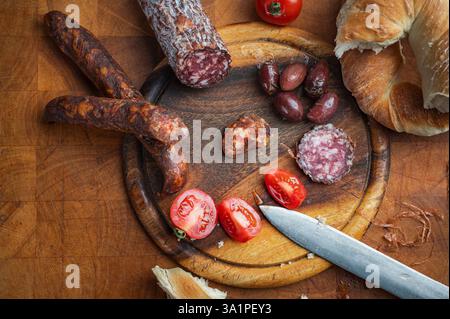 Salami, Wurst, Brot, Tomaten und Oliven auf einem Holzbrett, die die einfachen Freuden einer gemeinsamen Mahlzeit und kulinarischen Köstlichkeiten einfangen. Stockfoto