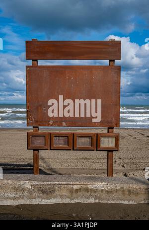 Am Strand steht ein Schild mit einem blauen Himmel im Hintergrund. Das Schild ist leer und hat einen rustikalen Look Stockfoto