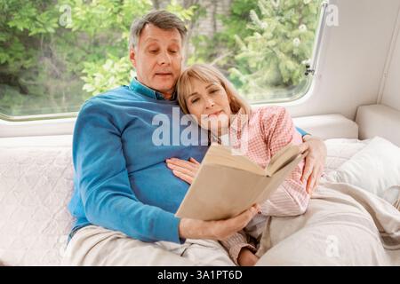 Familie Schlafenszeit Lesen. Liebevoller reifer Ehemann und Ehefrau mit Buch, das im Bett am Anhänger liegt Stockfoto