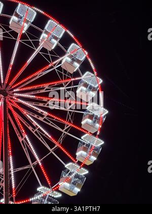 Nahaufnahme eines Riesenrads, beleuchtet mit roten und weißen Lichtern vor einem dunklen Nachthimmel Stockfoto