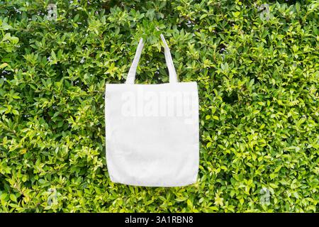 Leere Tragetasche aus Canvas auf grünem Laubhintergrund mit Kopierraum für Text oder Grafiken. Umweltfreundliche Tragetasche mit grünen Blättern auf dem Rücken in leuchtendem Petrol Stockfoto