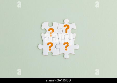 Das Bild zeigt vier weiße Puzzleteile, die auf einem hellgrünen Hintergrund miteinander verbunden sind. Jedes Stück hat ein orangefarbenes Fragezeichen, Stockfoto