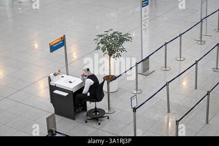 München, Deutschland. März 2025. In den frühen Morgenstunden sitzt ein Flughafenmitarbeiter am Terminal 2 am Flughafen München vor einem leeren Check-in-Schalter. Die gewerkschaft Verdi hat die Mitarbeiter des öffentlichen Dienstes und der Bodenabfertigung aufgefordert, am Montag einen 24-Stunden-Warnstreik auf 13 Flughäfen zu führen. Quelle: Peter Kneffel/dpa/Alamy Live News Stockfoto