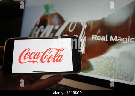 Roosendaal, Niederlande - 10. März 2025: Ein Mobiltelefon mit dem Logo von Coca-Cola, mit der Website des Unternehmens und dem Produkt im Hintergrund. Stockfoto