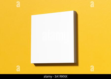 Minimalistische Komposition mit einer leeren weißen quadratischen Leinwand auf einer gelben Wand, ideal für die Präsentation von Kunstwerken oder Designs. 3D-Rendering. Stockfoto