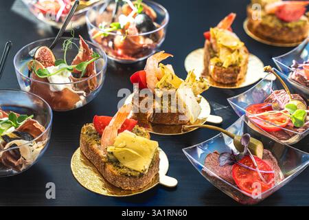 Catering-Buffet mit verschiedenen Snacks. Bruschetta mit Garnelen und Pesto-Sauce, Vitello Tonnato mit Ankerkerkerl und Rindfleisch auf einem schwarzen Tisch. Nahaufnahme. Stockfoto